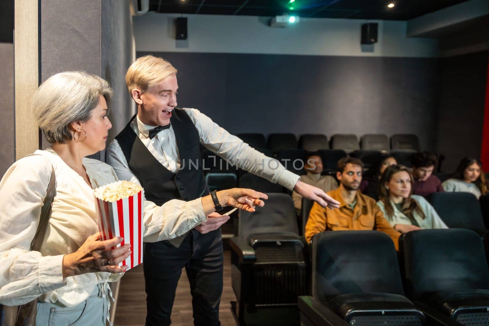 Movie theater employee showing available seats to a woman holding popcorn, ready to enjoy the film