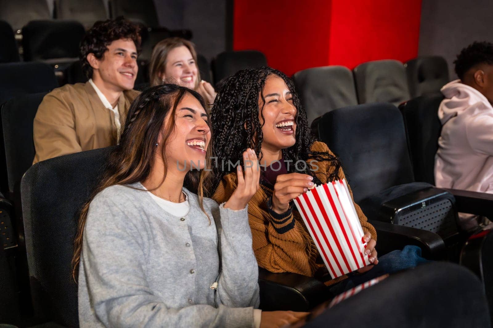 Friends enjoying a comedy film in a movie theater, laughing and sharing popcorn while soaking in the fun atmosphere of the evening