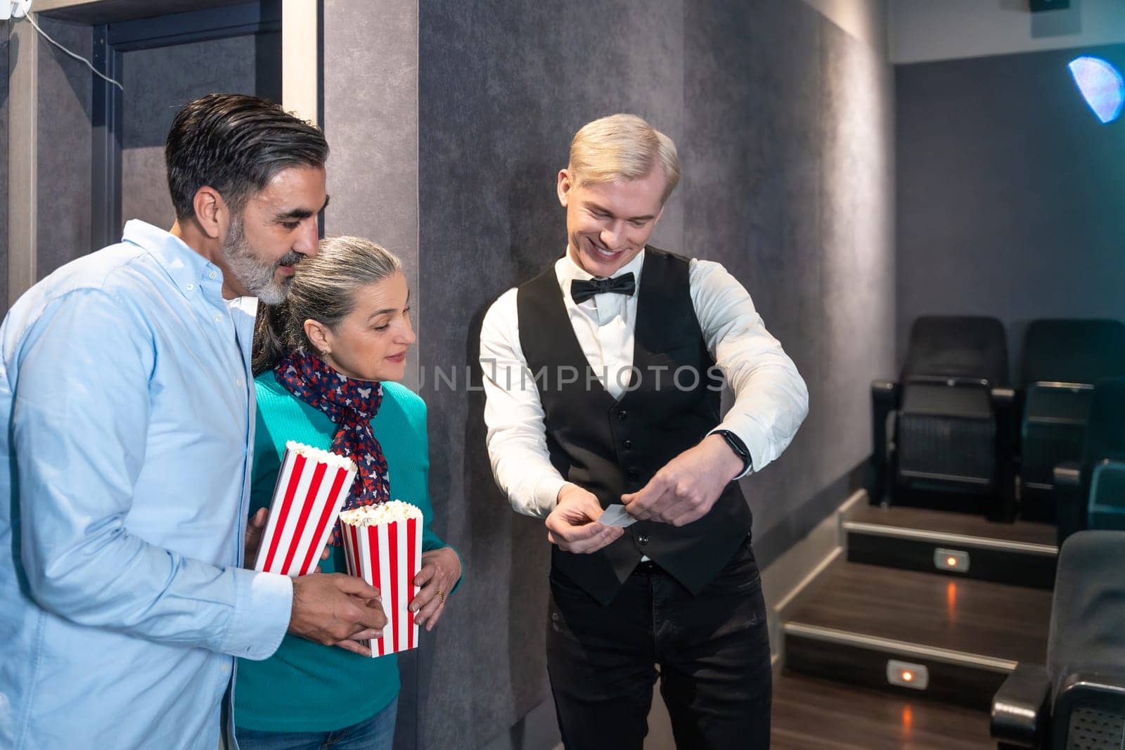 Couple entering a movie theater, holding popcorn buckets while the usher checks their tickets, enjoying a casual and happy evening together
