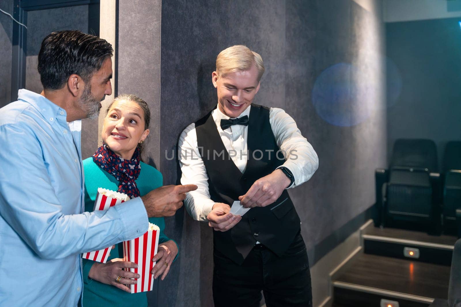 Couple holding popcorn buckets showing their tickets to the usher before entering the movie theater