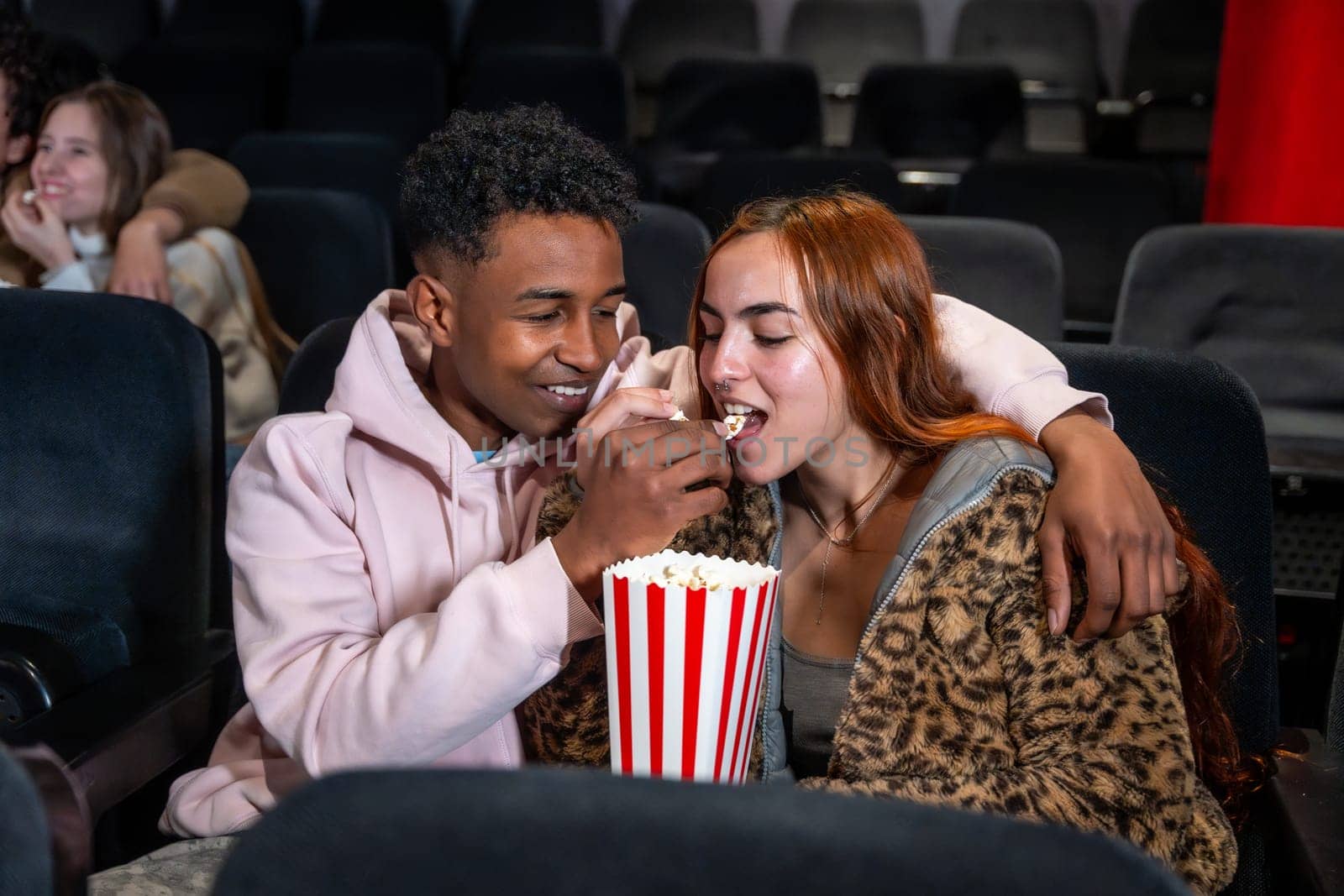 Young couple enjoys a movie date, sharing popcorn and a tender moment in the darkened theater