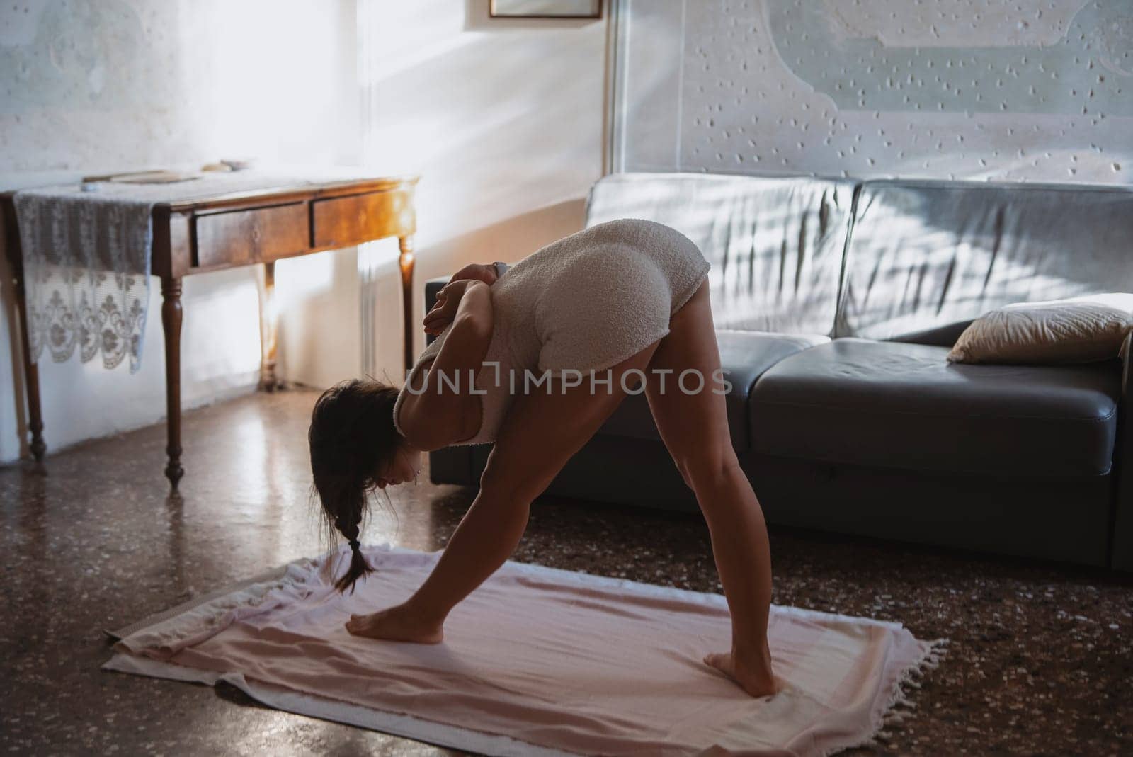 A woman is practicing yoga in a beautifully sunlit room, gaining focus on her flexibility and mindfulness
