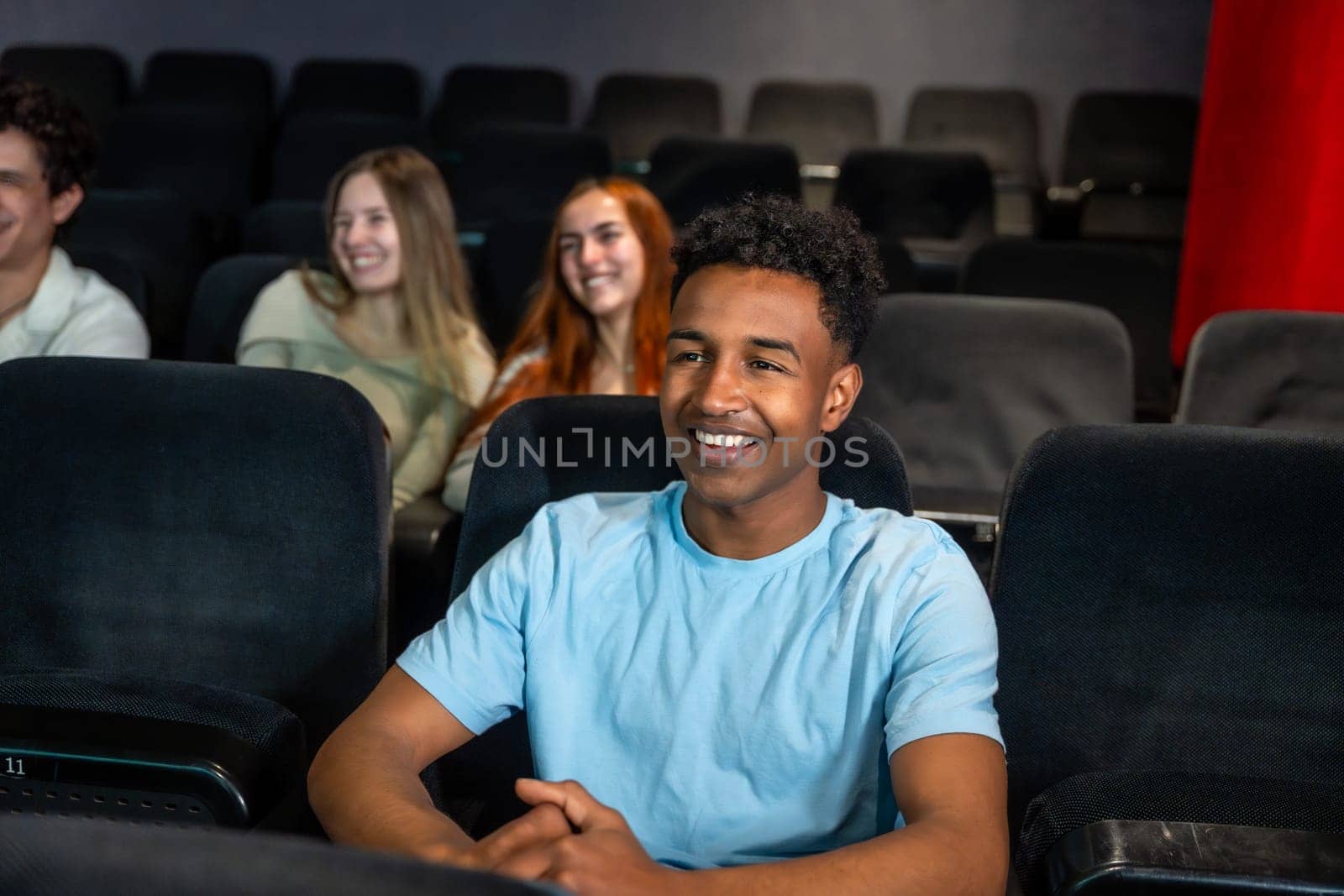 Young man smiles while watching a movie in a cinema, surrounded by his friends, enjoying a shared entertainment experience