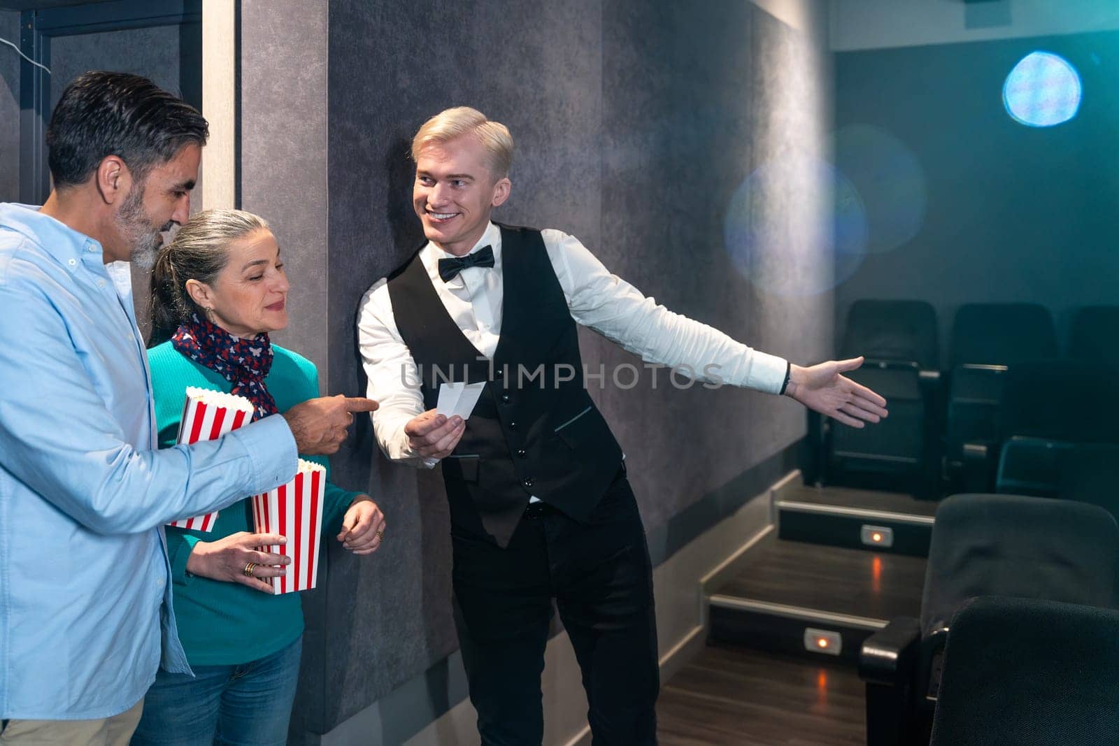 Movie theater usher showing seats to a couple holding popcorn buckets, ready to enjoy the film