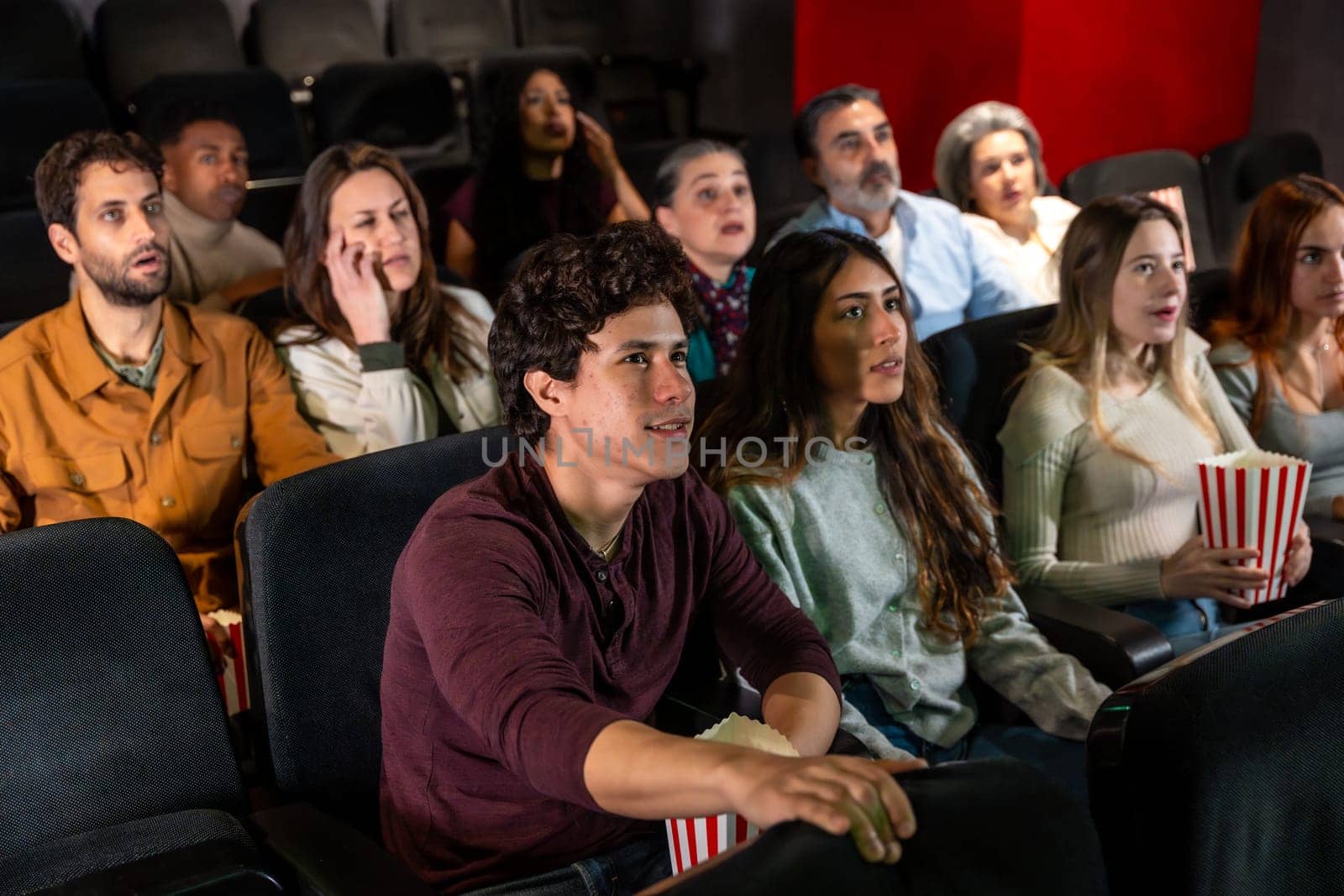 Captivated audience members of various ages and ethnicities experience a thrilling movie screening in a dark cinema, sharing moments of suspense and excitement