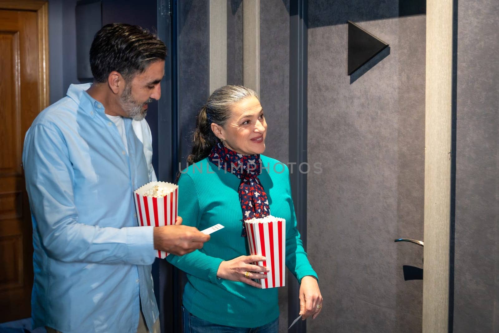 Happy mature couple entering cinema theater with popcorn and tickets, enjoying a night out together