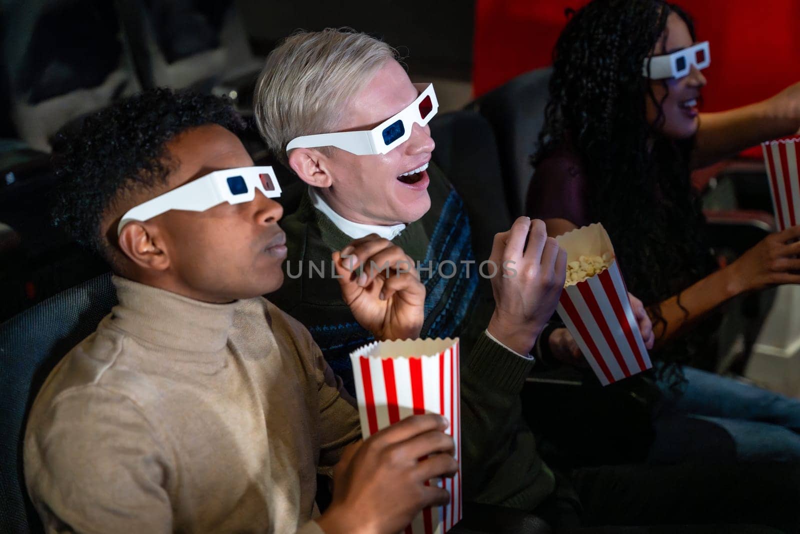 Young people wearing 3d glasses enjoying a movie at the cinema, eating popcorn and having fun together