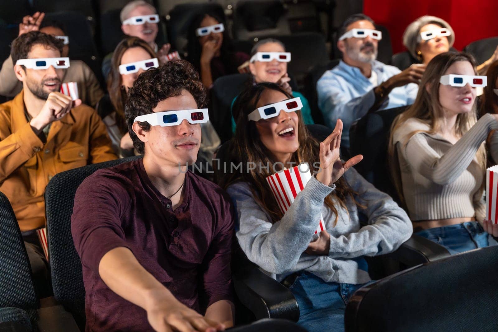Diverse group of friends wearing 3d glasses, watching a movie at the cinema and eating popcorn, having fun together