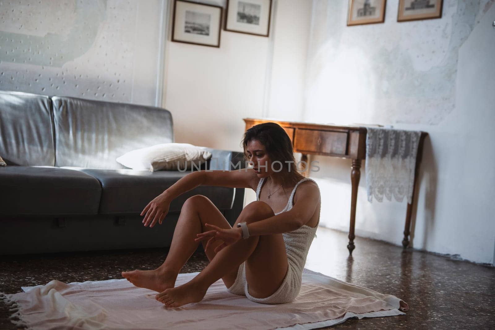 A woman gracefully poses in a thoughtful manner within a serene, minimalistic room that is filled with natural light