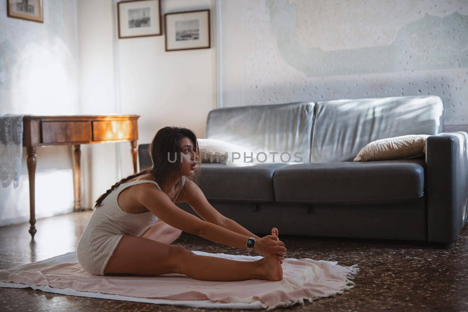 In a cozy living room, a woman stretches gracefully on a soft mat while fully engaging in her yoga practice