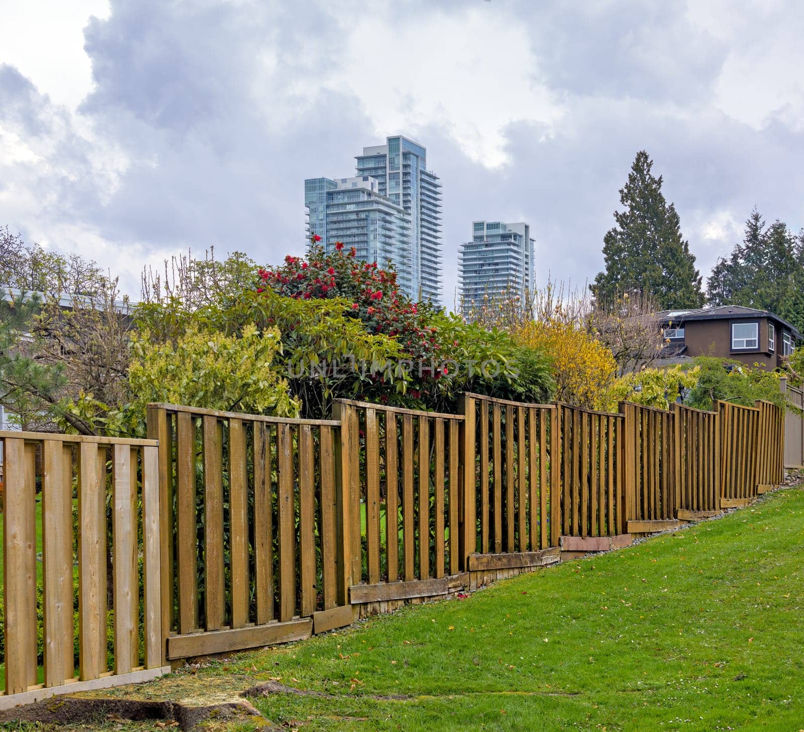Wooden fenc in residential area with high-rise buildings on cloudy sky background.
