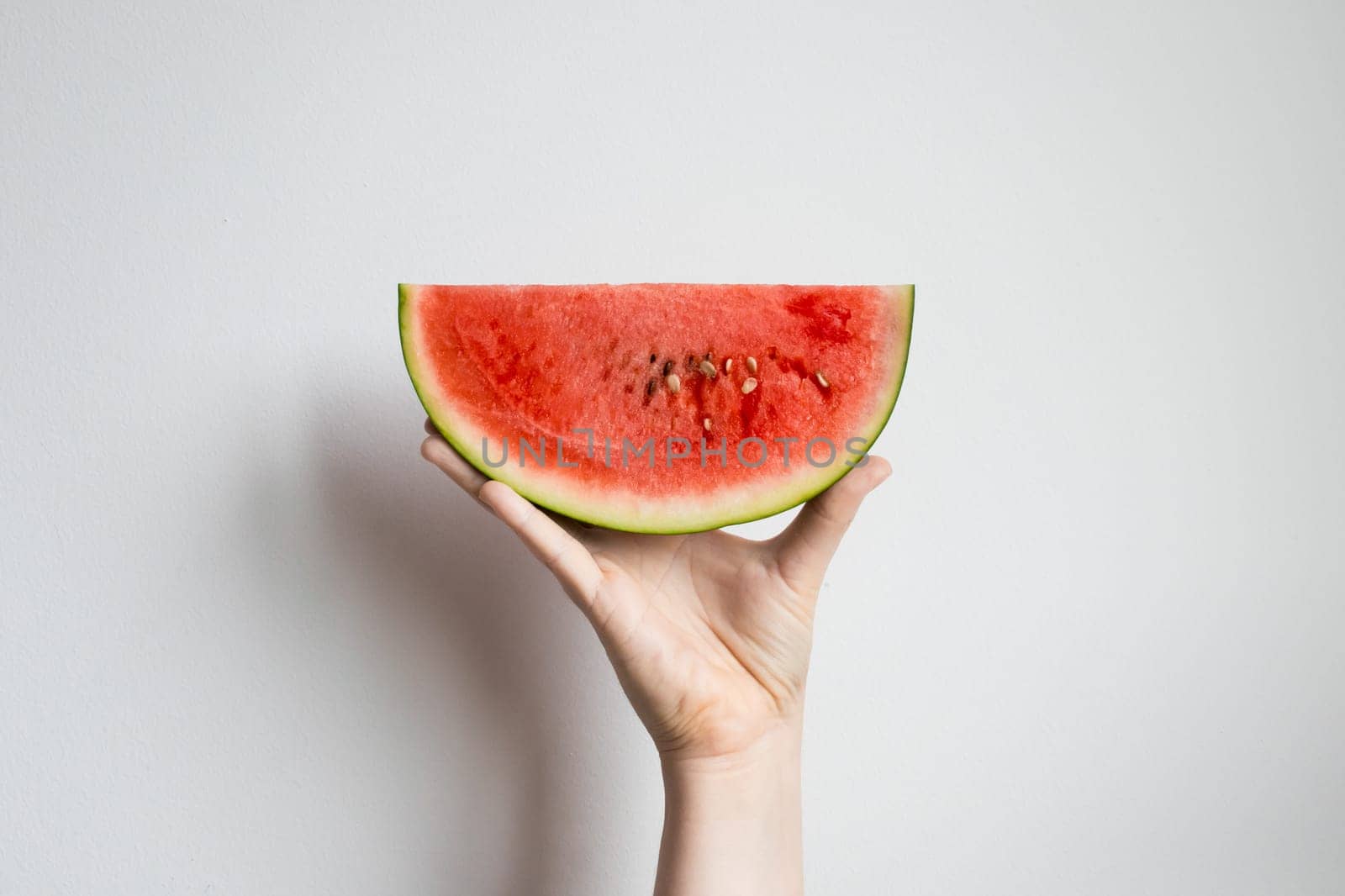 Hand holding a slice of fresh watermelon against white background.