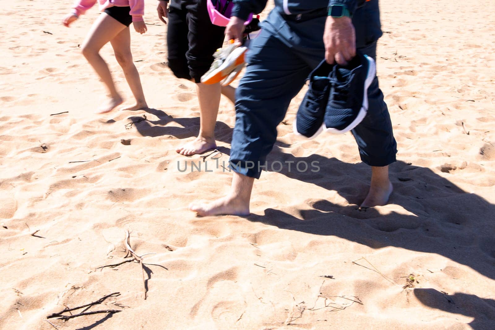 Group walking barefoot on sandy beach holding shoes.