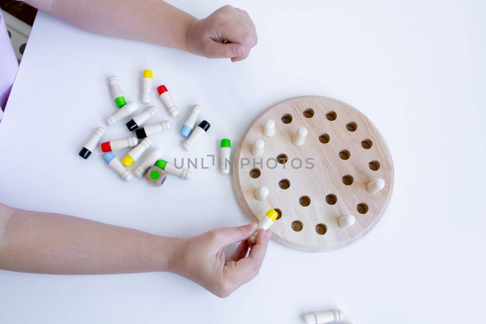 Child playing educational board game with wooden pegs and colored caps.