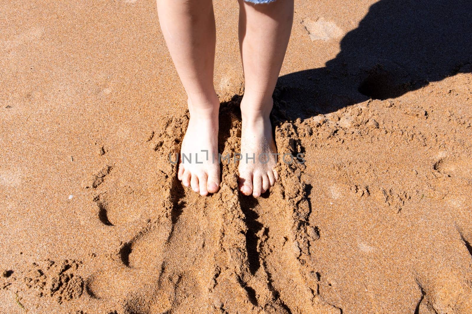 Feet of a young caucasian female on sandy beach in sunlight.
