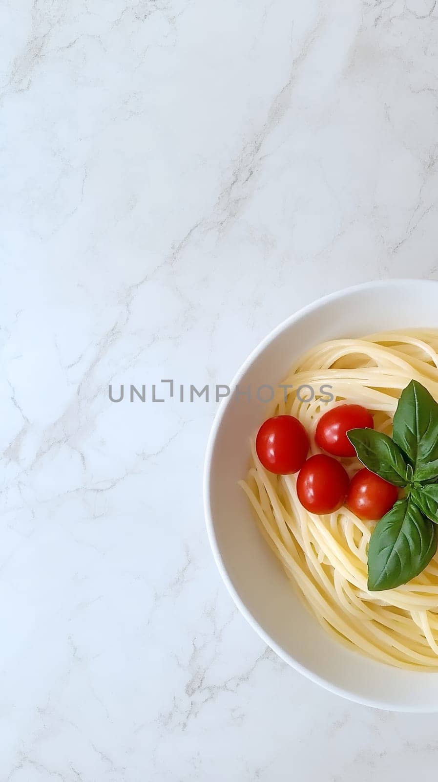A bowl of spaghetti garnished with fresh cherry tomatoes and basil leaves on a marble background with copy space.