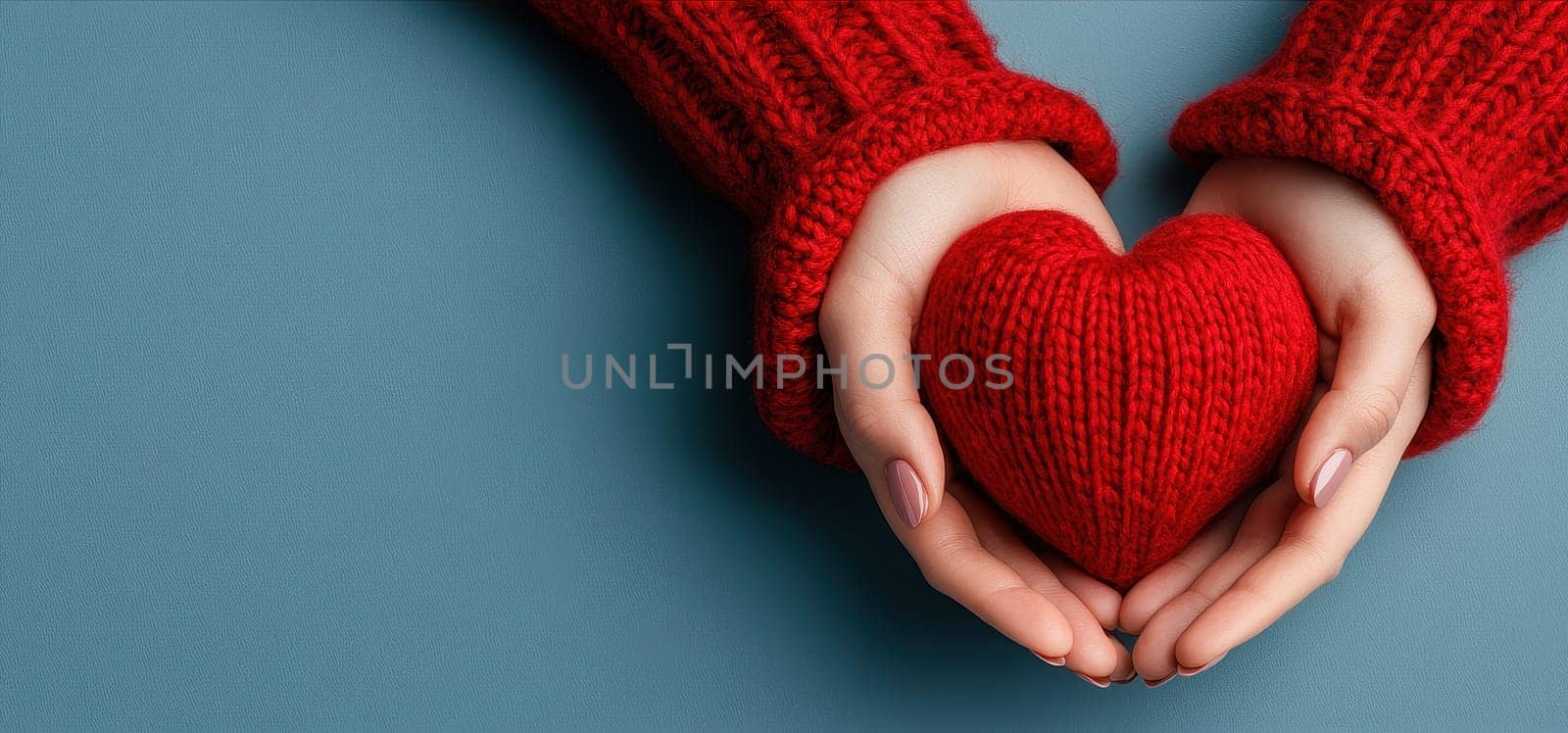 Warm hands in red knitted sweaters gently hold a red knitted heart, symbolizing love and care.