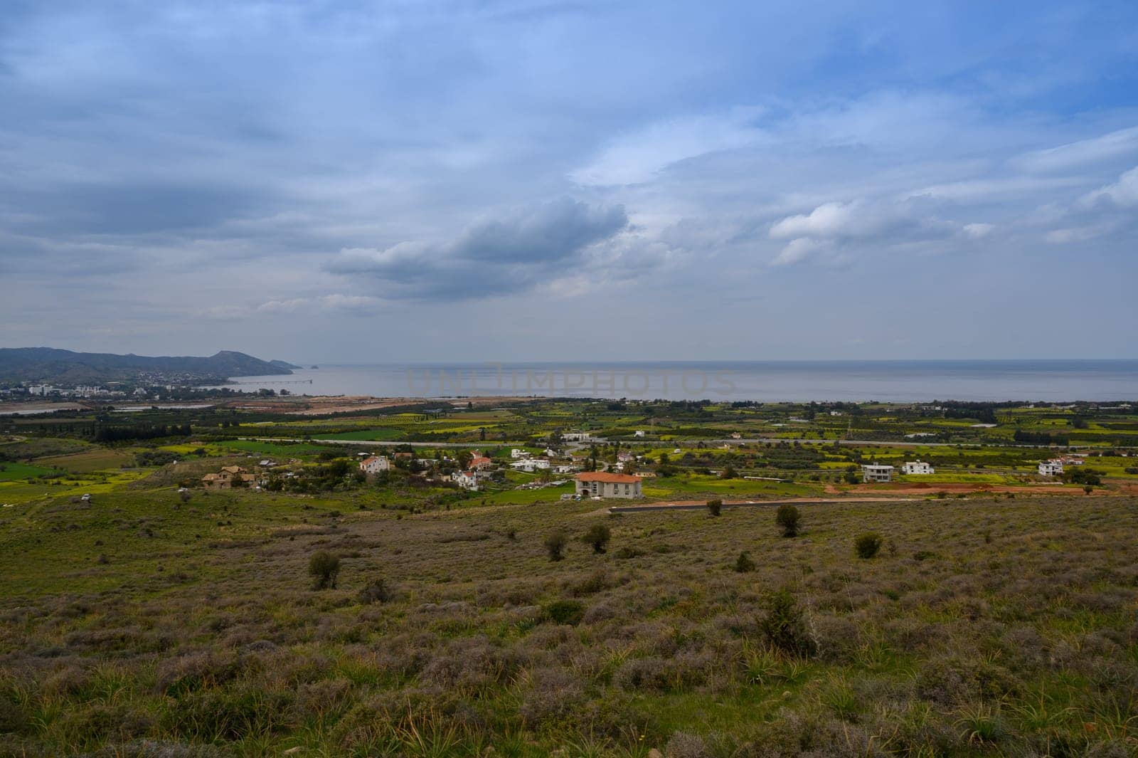 Rolling hills covered in soft greenery stretch toward the horizon, where fields meet the shimmering blue ocean.