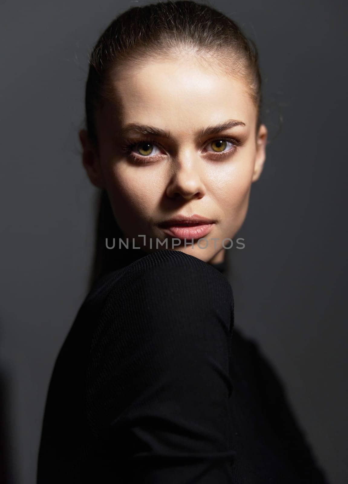 Striking female model showcasing elegance and self-assurance in a black turtleneck. Dark background highlights her features, emphasizing beauty and strength.