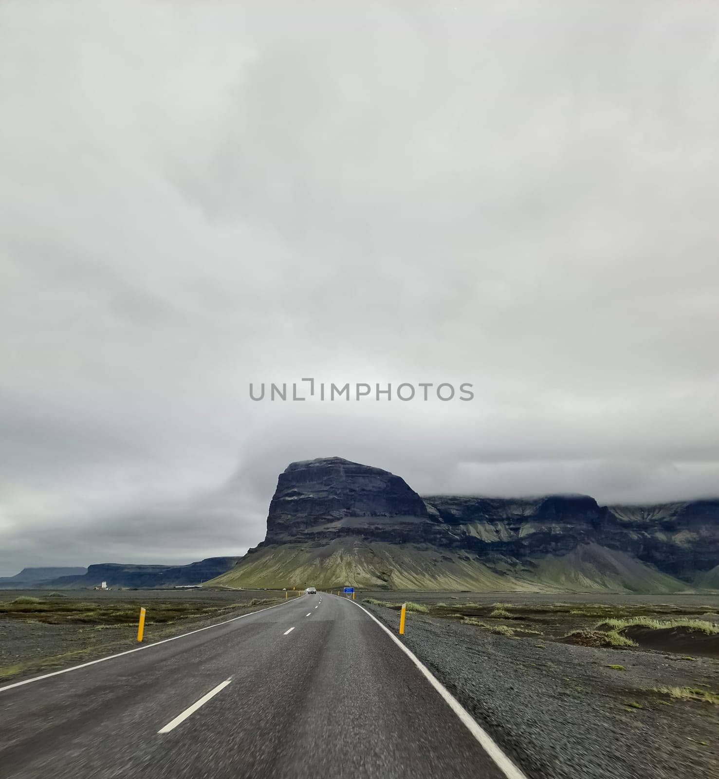 Asphalt road leading towards a large mountain in Iceland, under a cloudy sky, creating a dramatic and scenic view