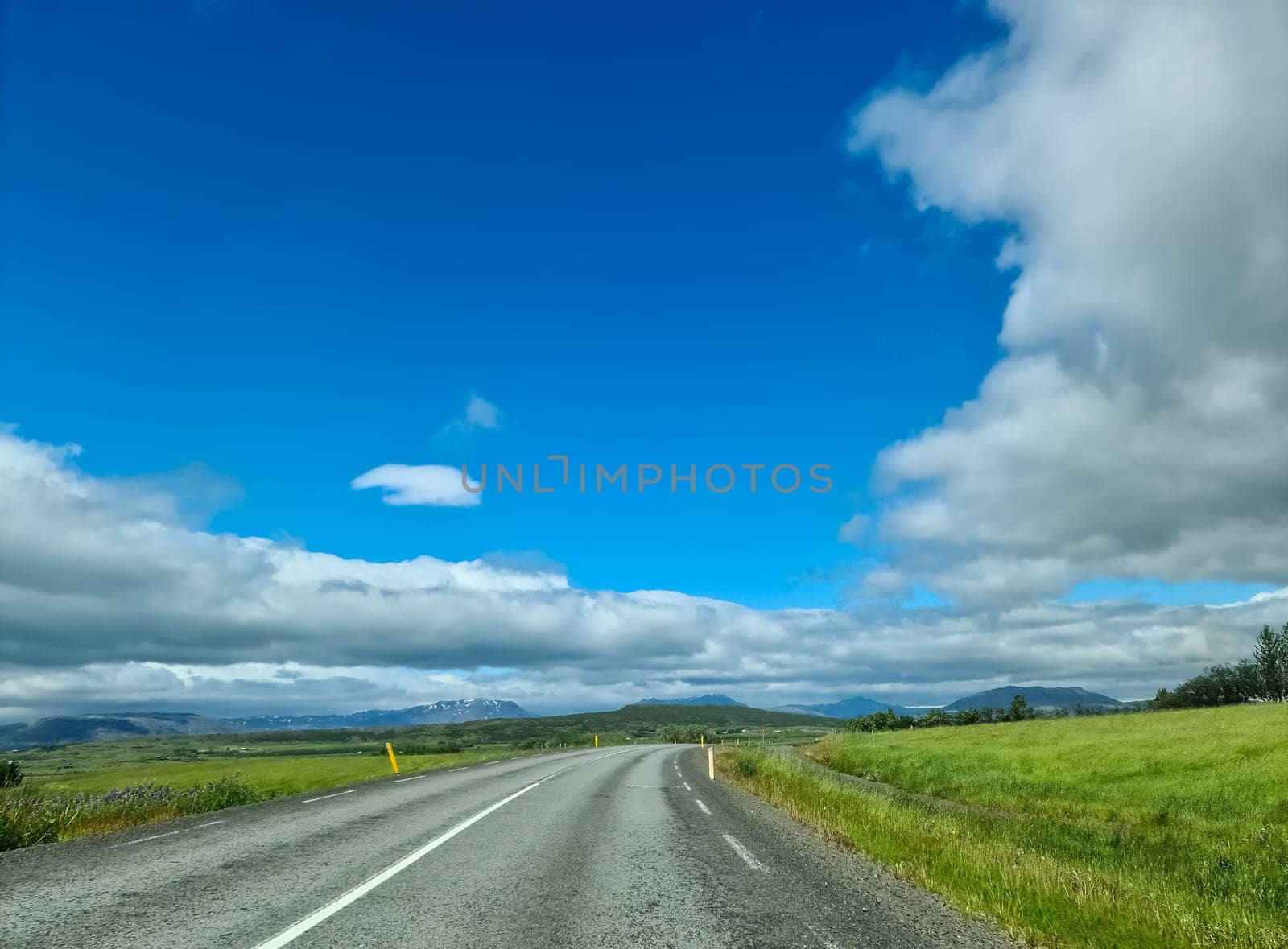 Long straight asphalt road crossing the Iceland countryside under a beautiful cloudy blue sky