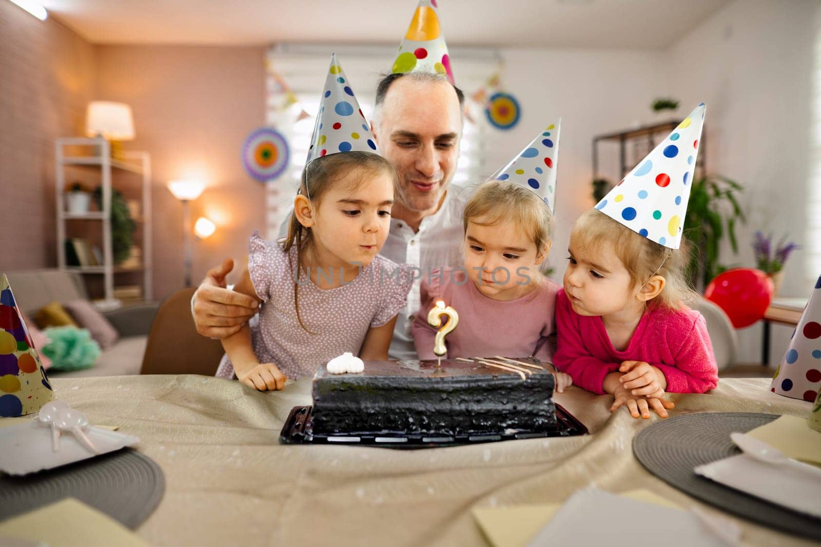 Children gather around a cake, ready to make a wish and blow out candles.
