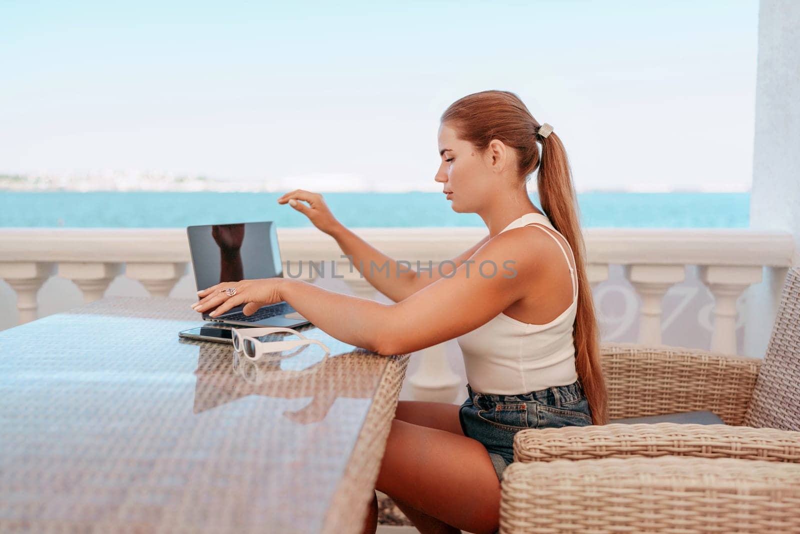 Woman coffee cafe laptop sea. Female freelancer using laptop on coffee break in modern cafe with sea view in the morning.