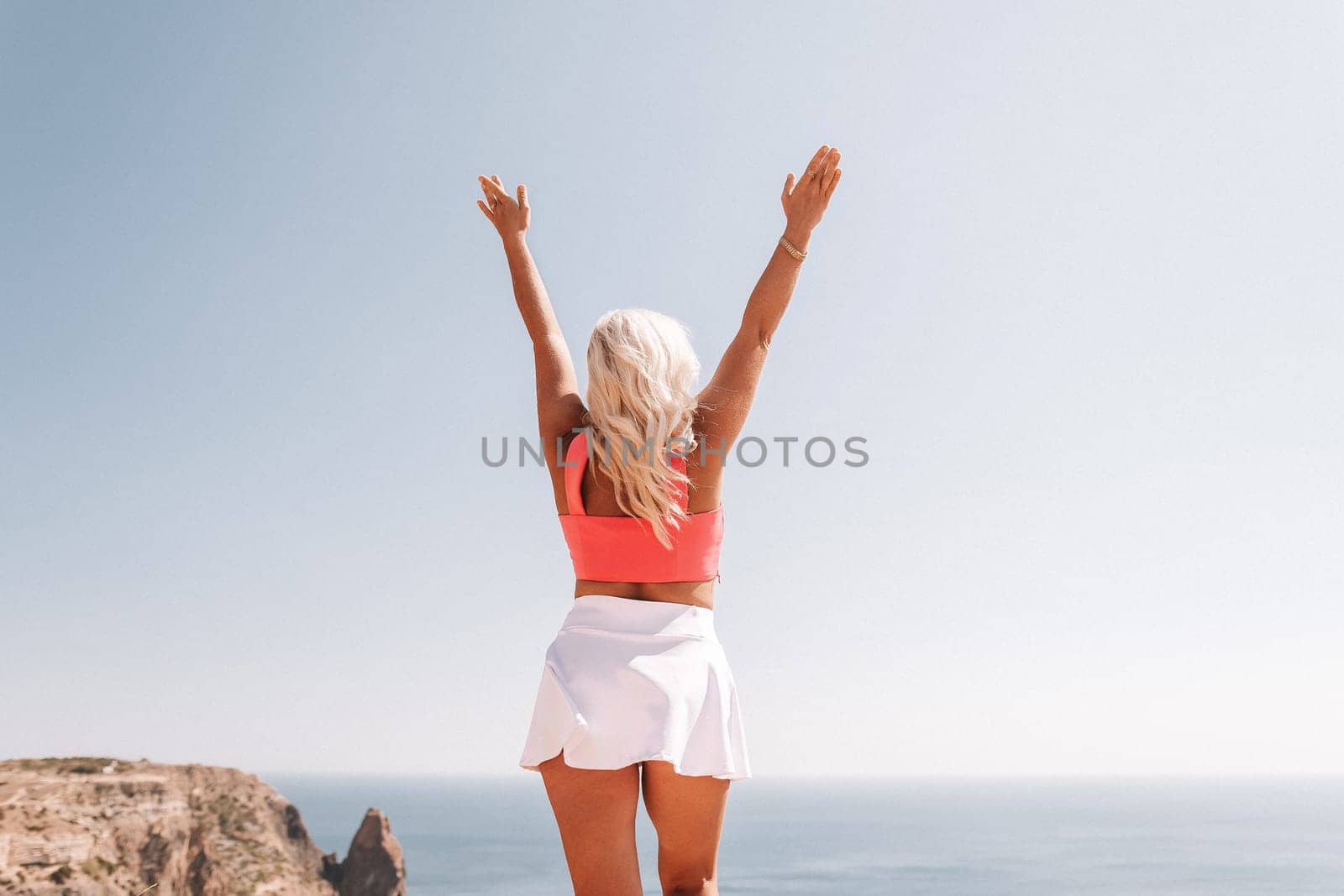 A woman in a pink top and white skirt is standing on a beach, looking up at the sky