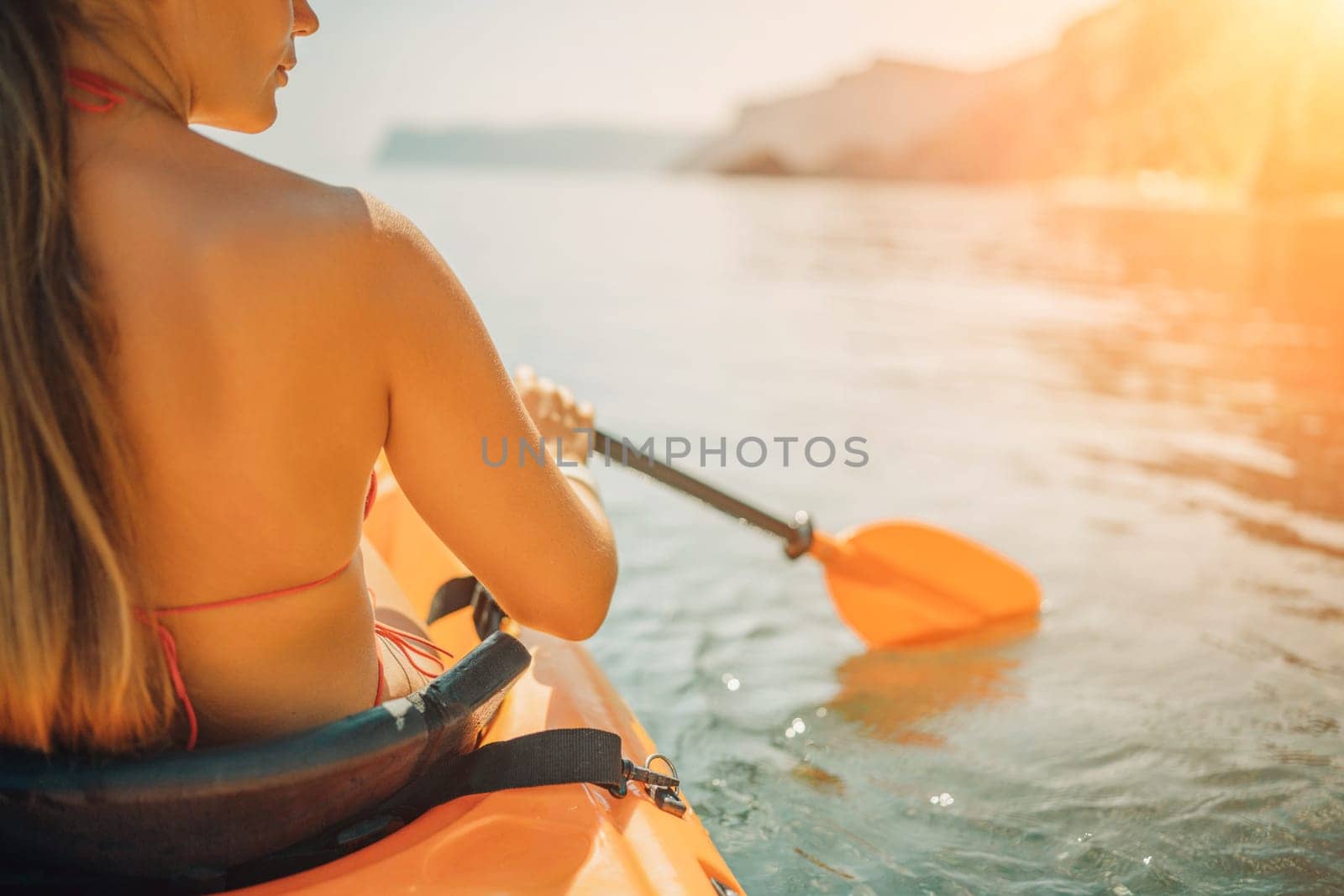 Woman in kayak back view. Happy woman with long hair in a swimsuit and hat floating in kayak on the sea. Summer holiday vacation. Summer holidays vacation at sea