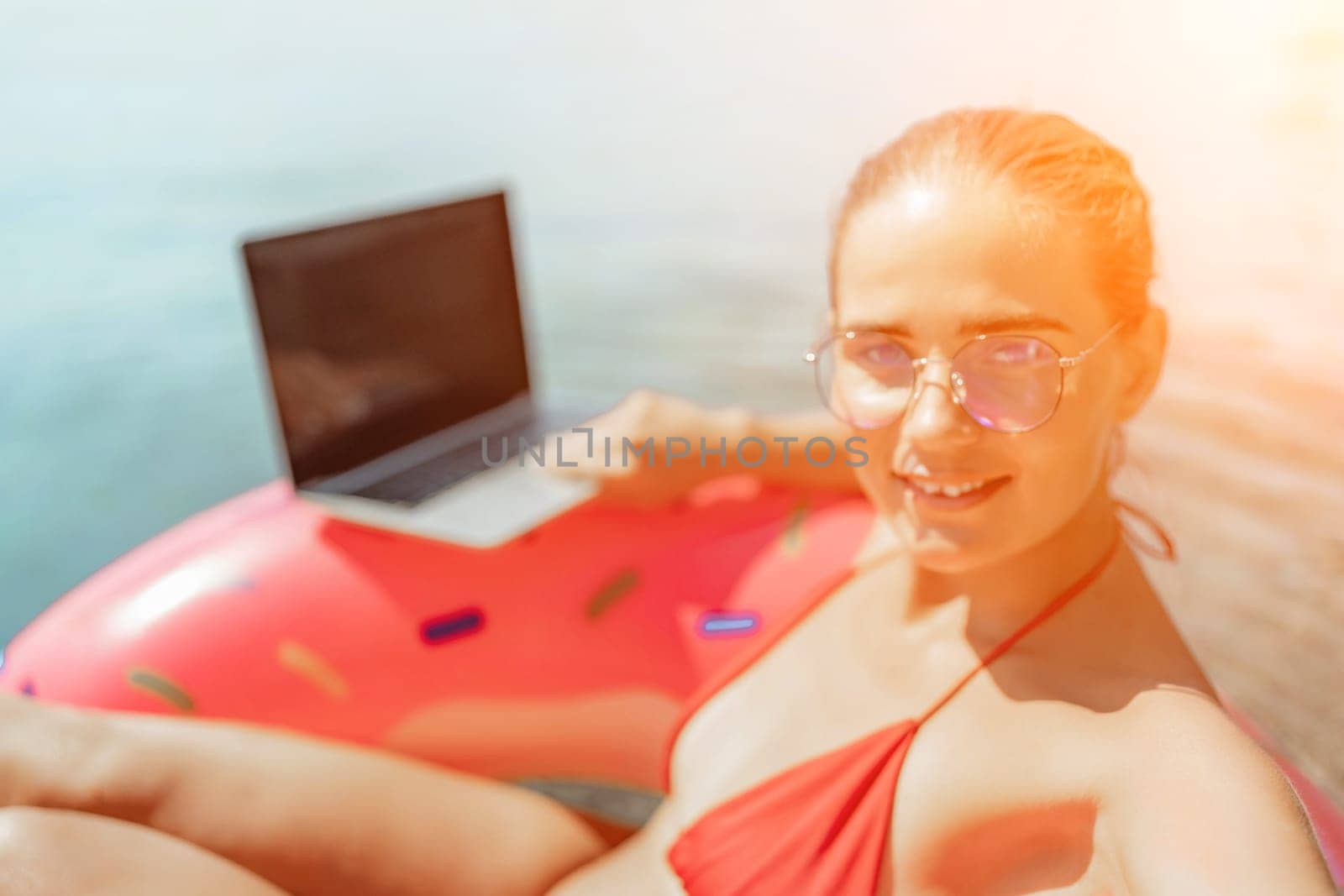 Woman laptop sea. Freelancer woman in sunglases floating on an inflatable big pink donut with a laptop in the sea. People summer vacation rest lifestyle concept