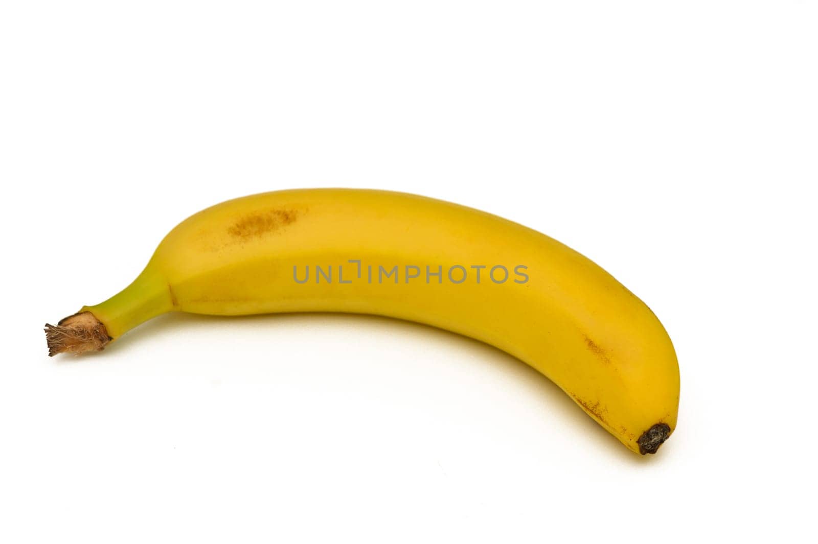 One curved yellow banana sits elegantly on a pristine white surface, embodying freshness with its vibrant color. This tropical fruit offers a delightful essence to snacks and meals.