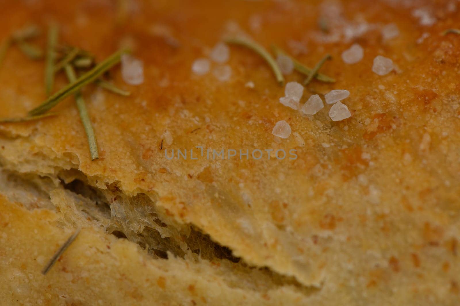 Warm bread emerges from the oven, golden and inviting, topped with aromatic herbs and sea salt that enhance its flavor. A perfect treat for any meal.