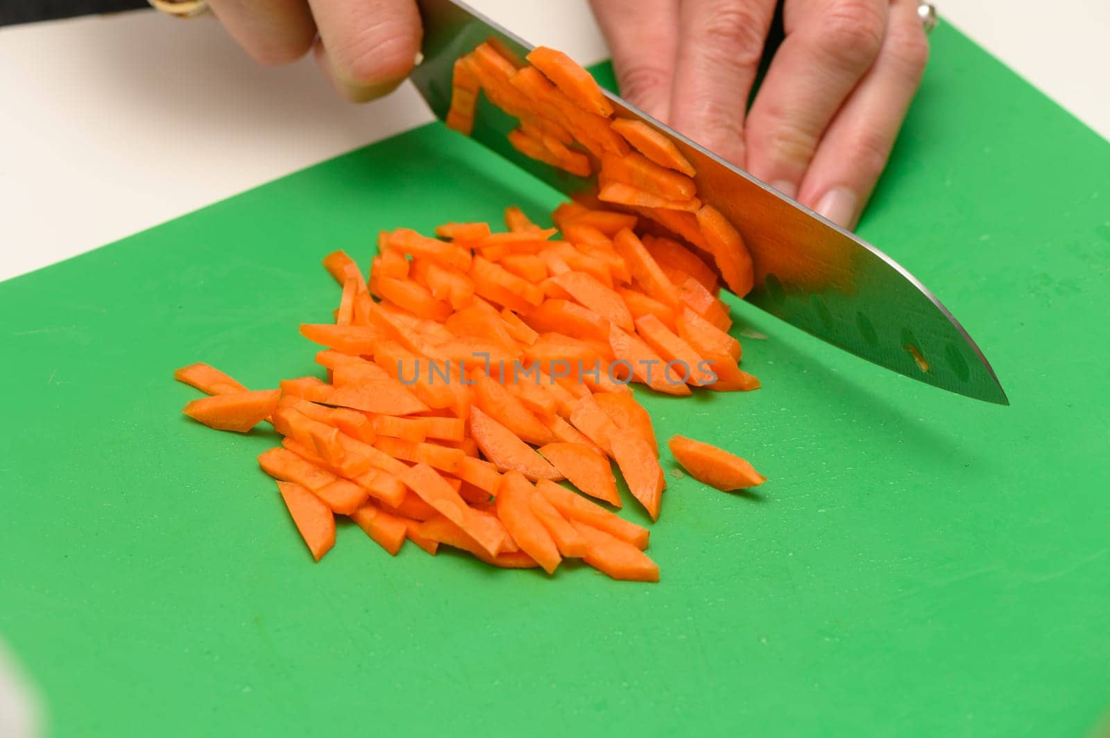 Diligent hands maneuver a sharp knife, expertly chopping fresh orange carrots on a bright green cutting board, ready for a delicious meal. Precision and care shine in the kitchen.