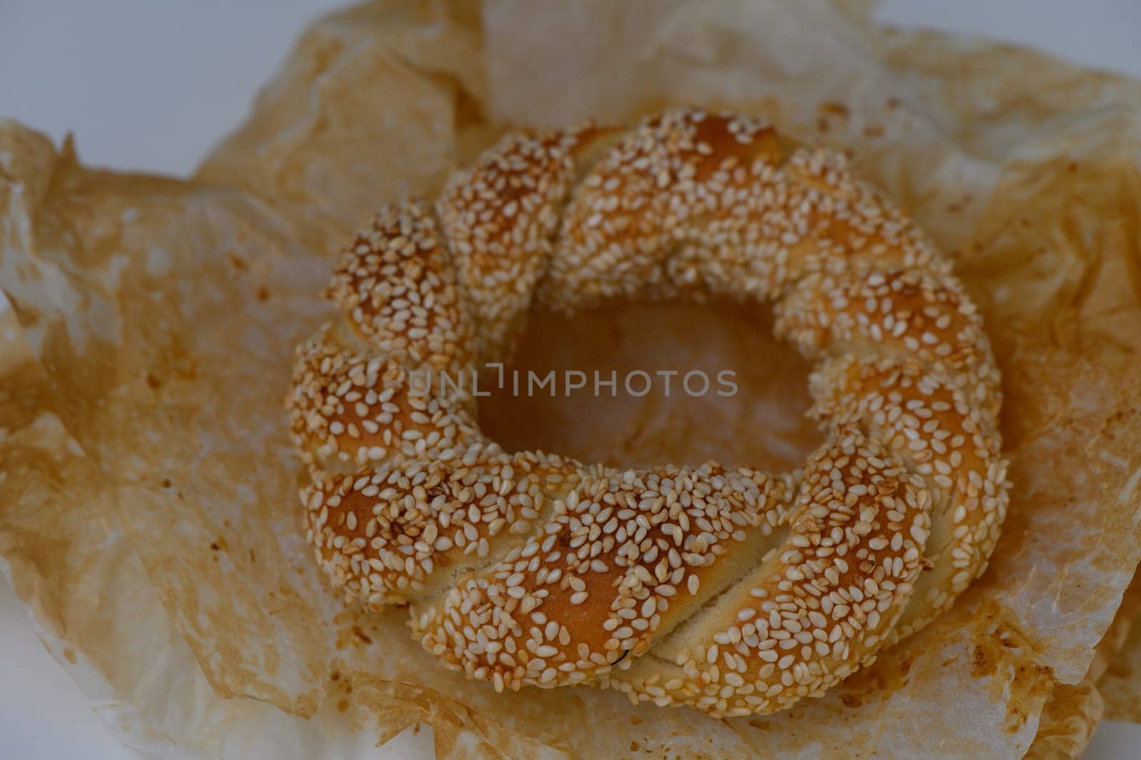 Delight in the warm, inviting aroma of freshly baked sesame bread, showcasing a braided shape on soft, crumpled paper, perfect for sharing during a relaxed afternoon gathering.
