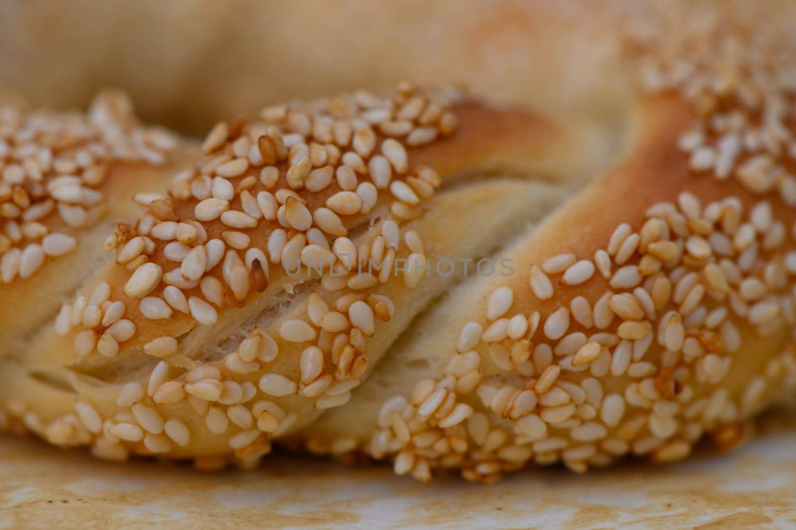 Delicate strands of braided bread glisten with a coating of toasted sesame seeds, highlighting the craft of baking. Sunlight bathes the warm creation, inviting all to savor its flavor.