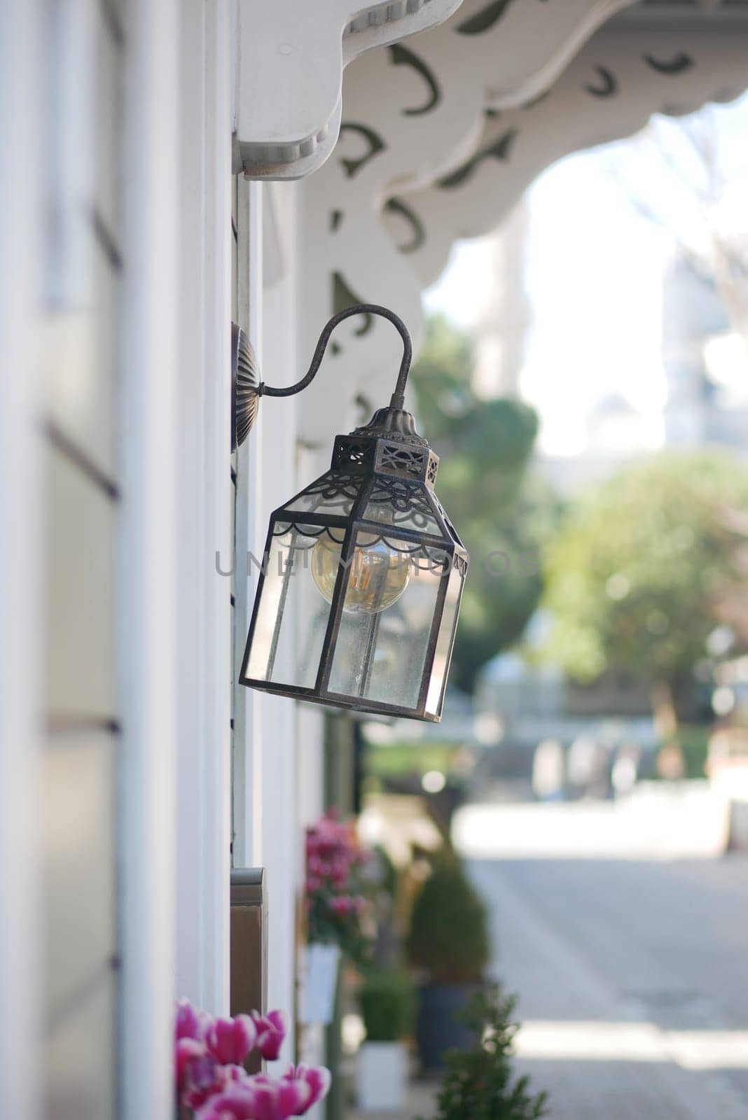 A stylish street lamp hangs beside a vibrant flower display on a sunny day.