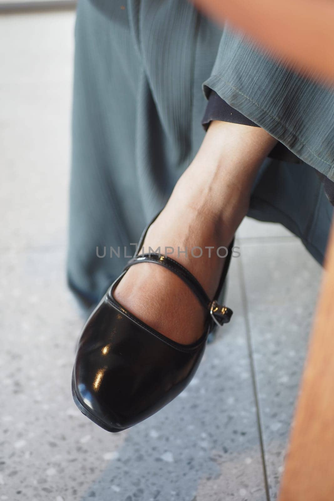 A person in a long skirt sits, showcasing a black strap shoe on their foot.