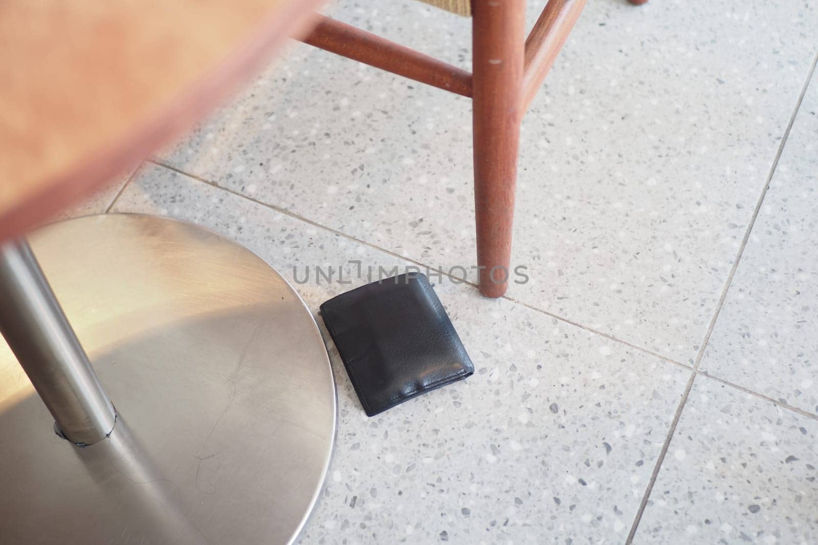 A black wallet lies on the floor beside a wooden table.