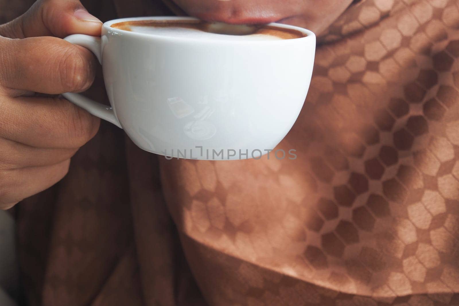 A person sips coffee while wearing a brown scarf in a relaxed atmosphere.