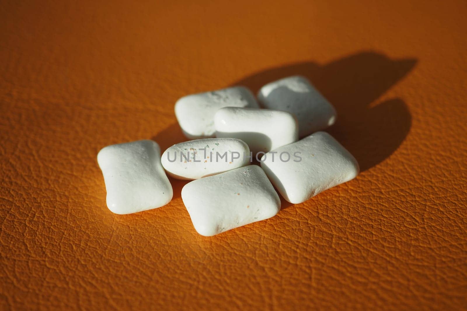 Several white chewing gum pieces are laid out on a textured orange surface.