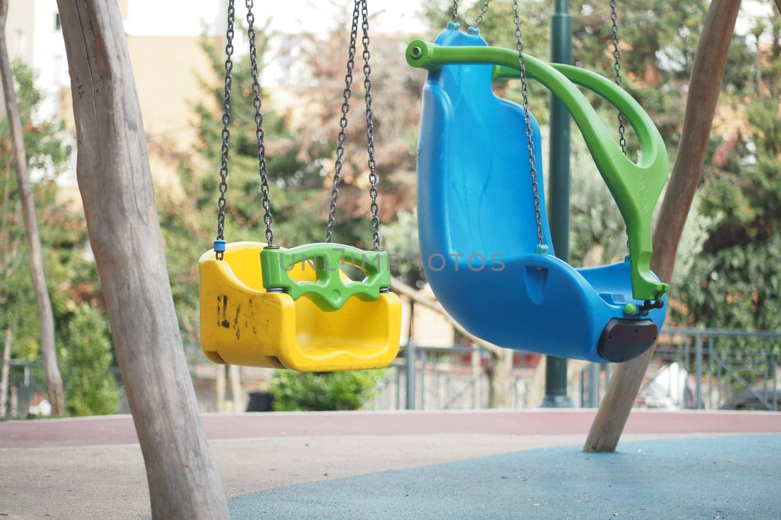 Two swings in bright colors hanging from sturdy chains in a park setting.