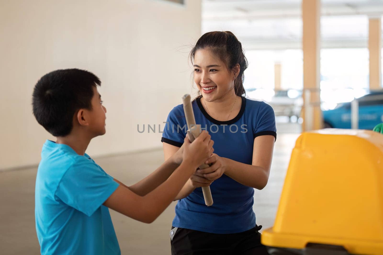 A woman guides a boy on how to dispose of plastic correctly, emphasizing the importance of teamwork and environmental responsibility.