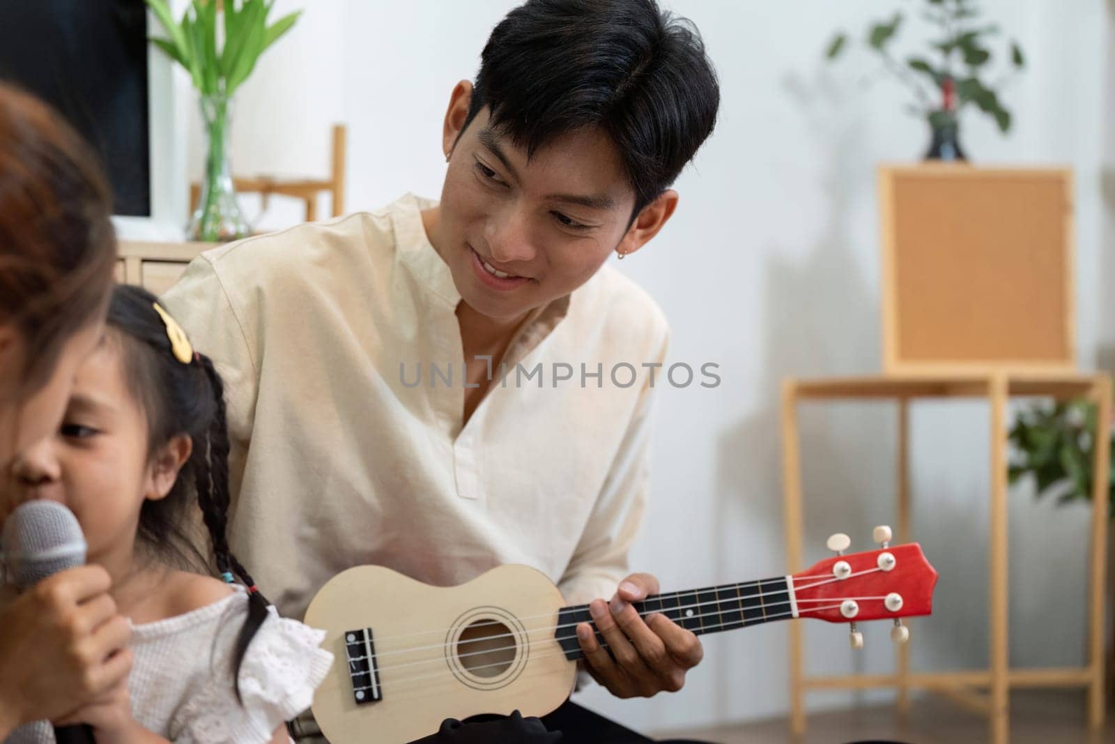 A proud father listens intently as his young daughter sings into a microphone, highlighting the bond formed through family music activities.