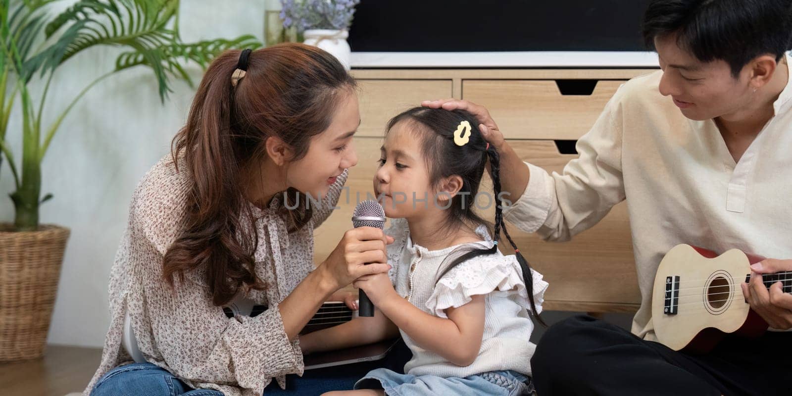 A joyful family moment where a little girl sings into a microphone while her mother plays the ukulele, fostering creativity and connection.