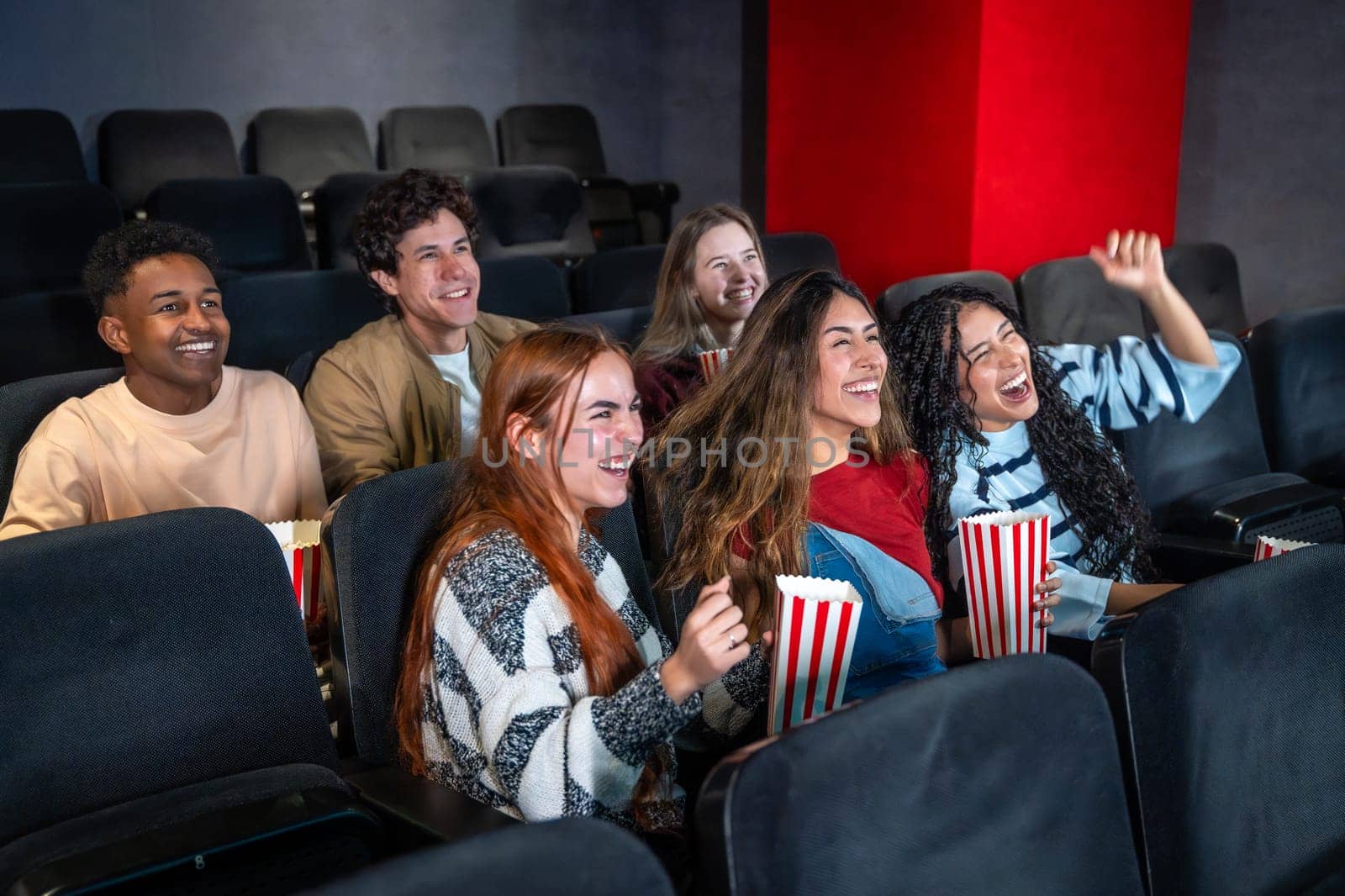 Young people having fun watching a film at the movie theater, eating popcorn and laughing
