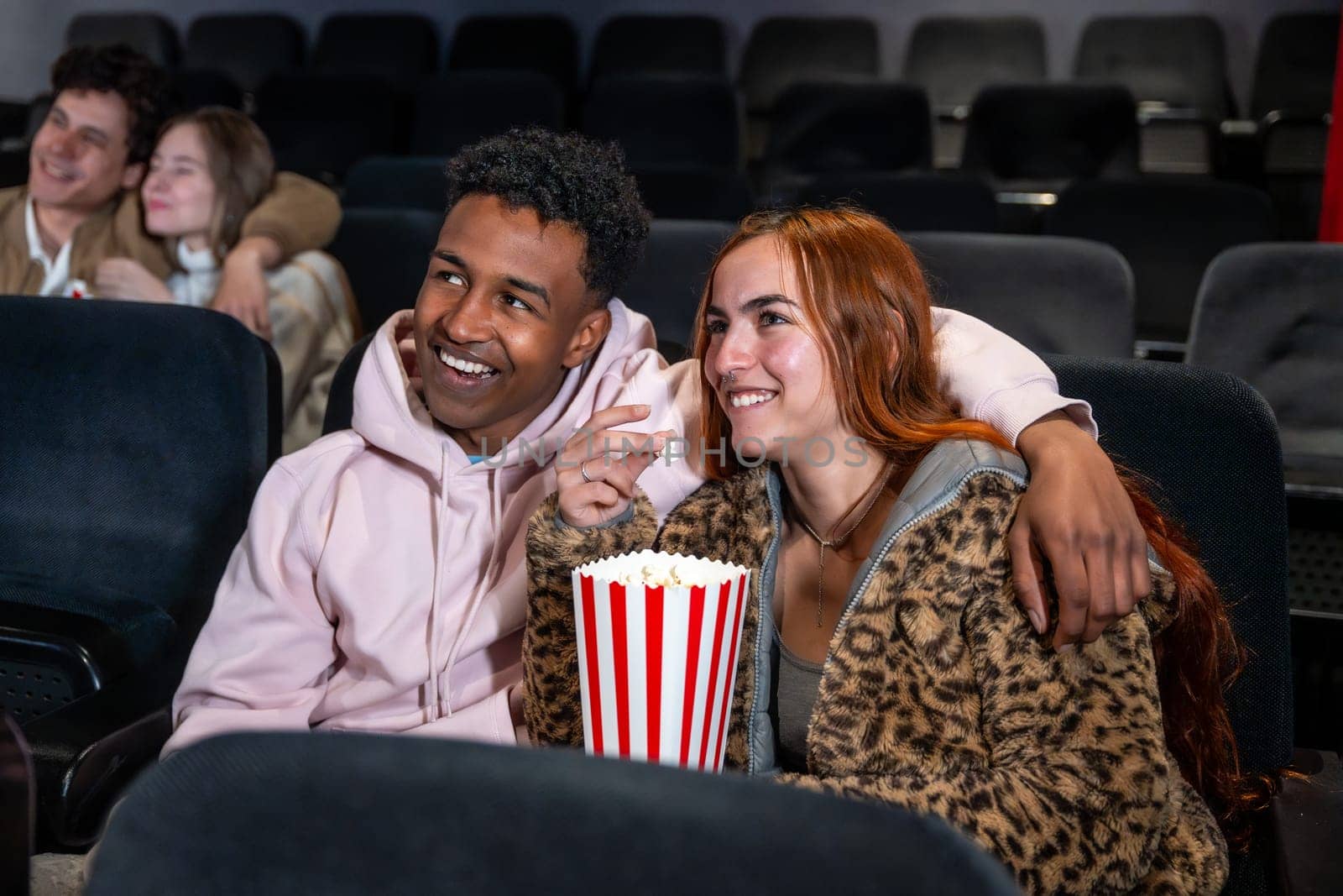 Happy couple sharing popcorn while watching a movie at the cinema, enjoying a night out with friends