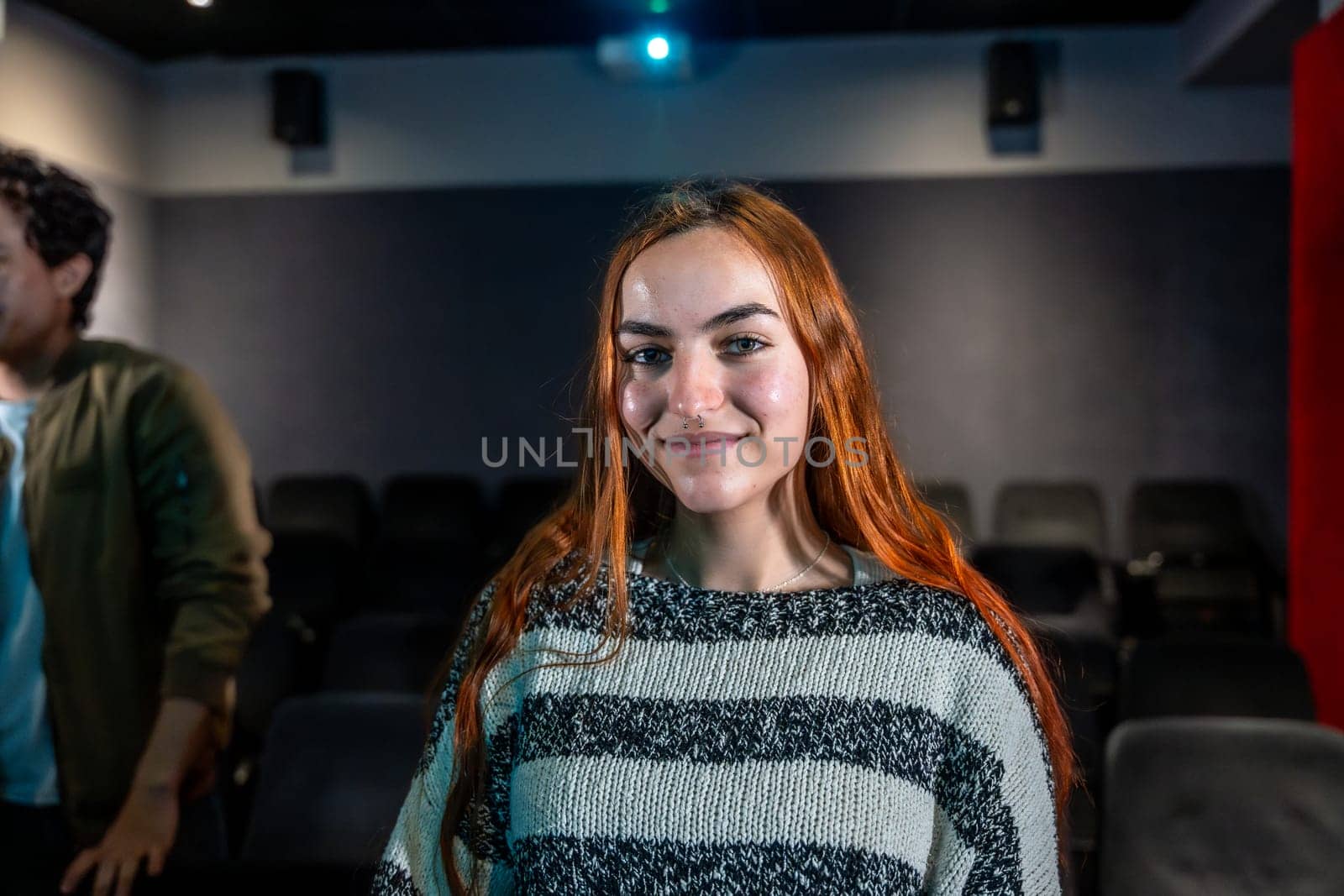 Redhead young woman smiling during movie session in a cinema theater, audience in the background