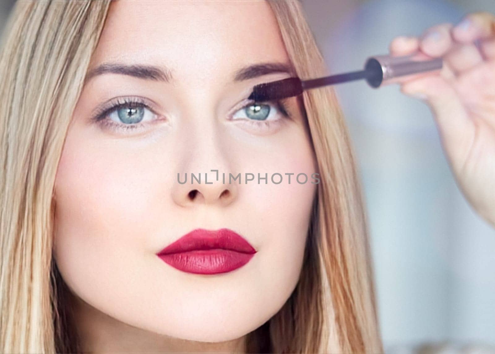 Woman applying mascara with confidence, defined brows and red lipstick. Blonde beauty focused on her eye makeup, cosmetics look