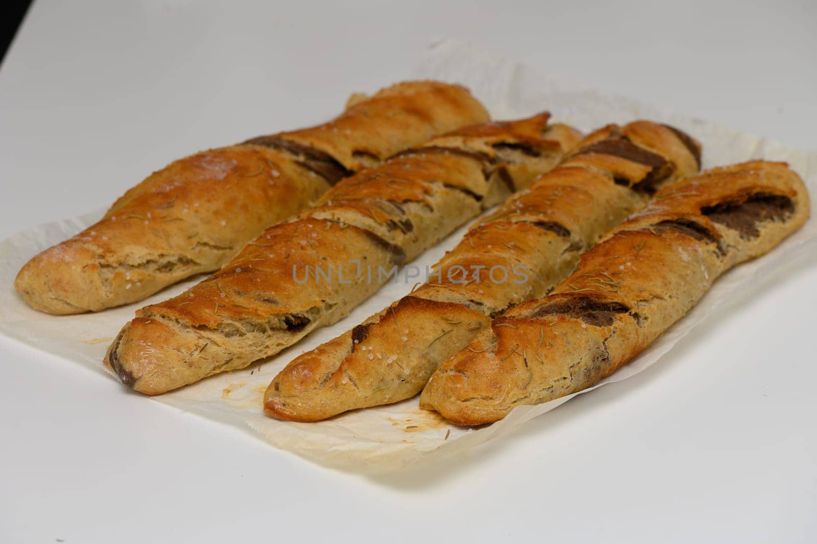 Three long, crusty bread loaves rest on parchment, their golden-brown exterior hinting at a delicious, warm interior. The kitchen setting is bright, inviting culinary creativity.