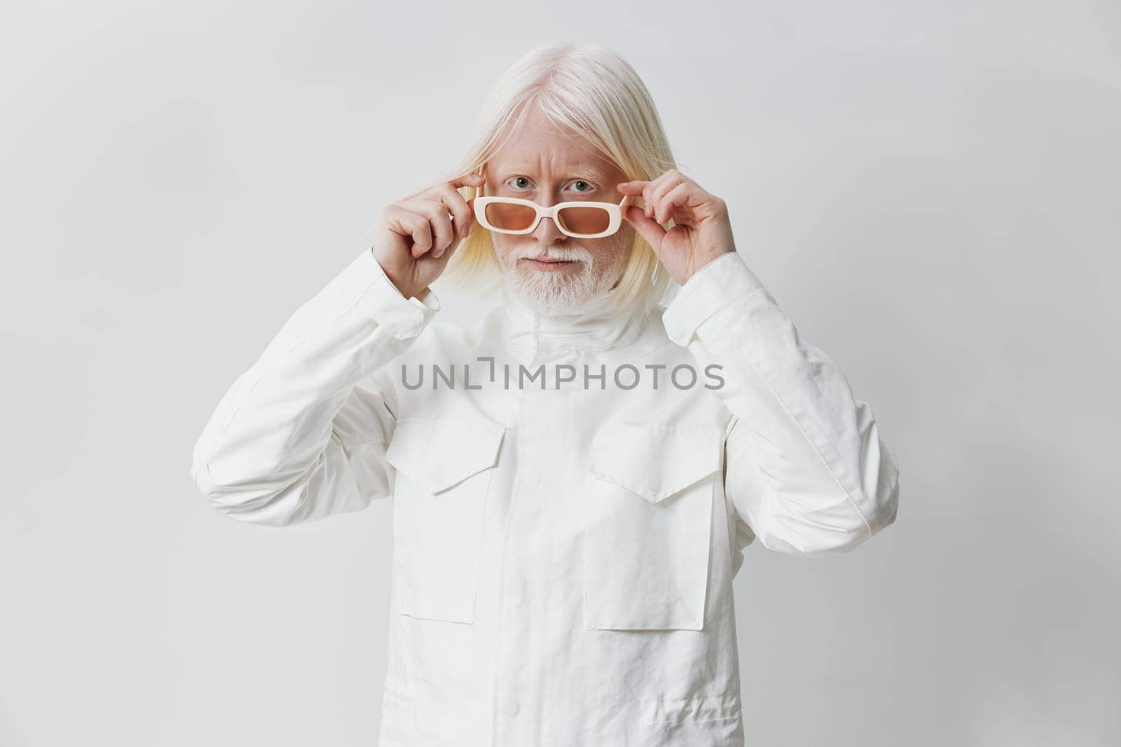 This image features a fashionable older man with long white hair and a beard, adjusting his clear glasses while wearing a white jacket The minimalist white background highlights his stylish look, expressing confidence and modernity